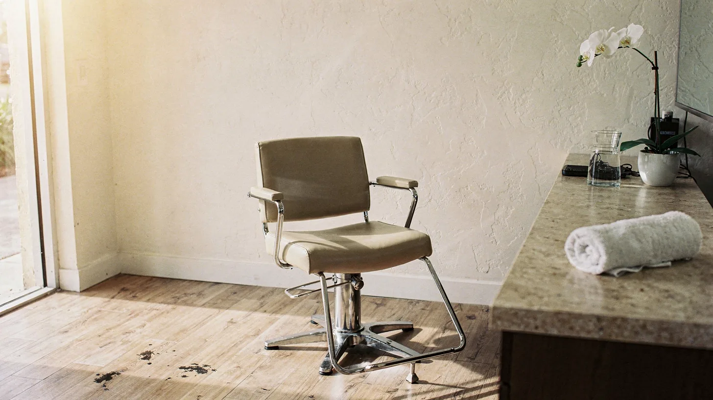 The quiet reception corner of a small Naples salon, with an empty styling chair, a folded towel and a white orchid on a stone counter
